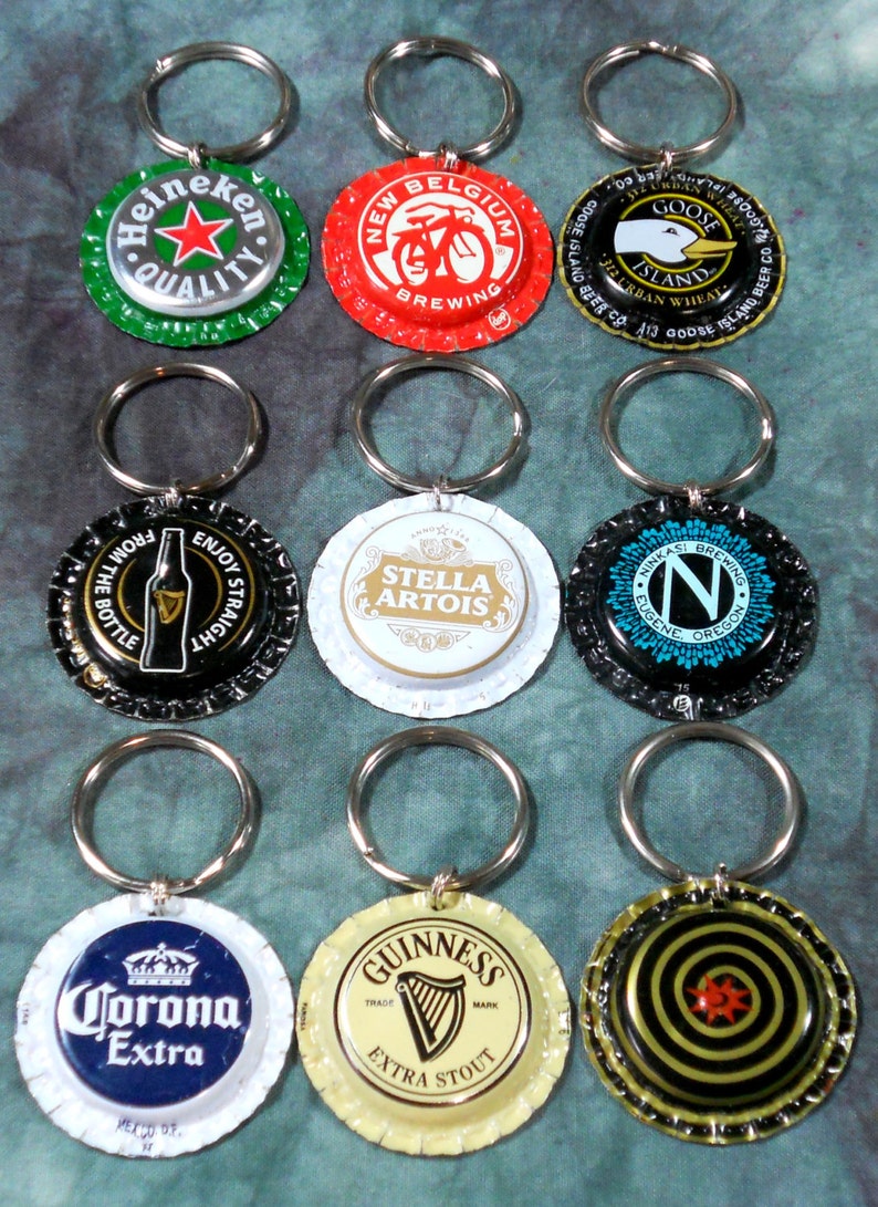 May include: A collection of bottle cap keychains featuring various beer brands. Keychains include Heineken, New Belgium Brewing, Goose Island, Stella Artois, and Guinness. Each cap is attached to a silver keyring.