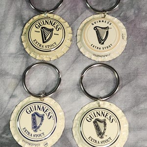 Pu&ograve; includere: Quattro portachiavi con tappo di bottiglia Guinness Extra Stout. Ogni portachiavi presenta un anello in metallo argentato attaccato a un tappo di bottiglia con il logo Guinness, un'arpa e le parole "Extra Stout". I tappi sono bianco sporco con testo nero e blu.