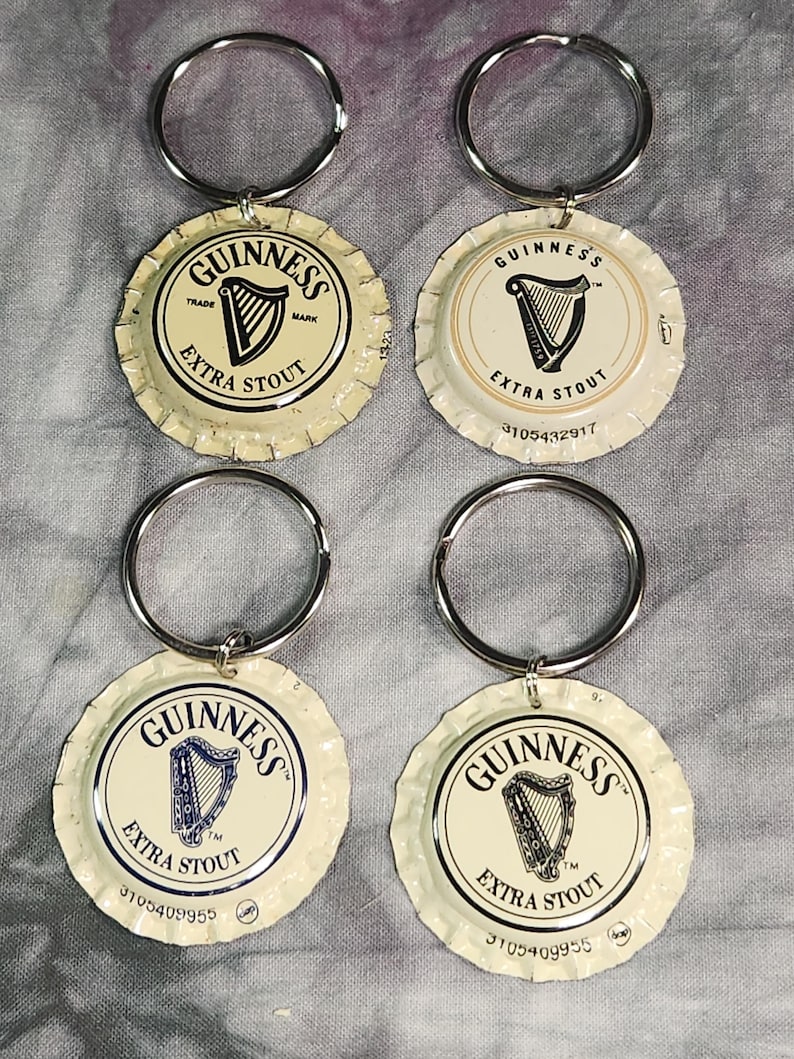 Pu&ograve; includere: Quattro portachiavi con tappo di bottiglia Guinness Extra Stout. Ogni portachiavi presenta un anello in metallo argentato attaccato a un tappo di bottiglia con il logo Guinness, un'arpa e le parole "Extra Stout". I tappi sono bianco sporco con testo nero e blu.