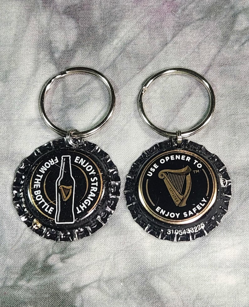 Pu&ograve; includere: Due portachiavi a forma di tappo di bottiglia. Uno presenta una grafica di bottiglia con la scritta "FROM THE BOTTLE ENJOY STRAIGHT". L'altro ha una grafica di arpa con la scritta "USE OPENER TO ENJOY SAFELY". Entrambi hanno portachiavi argentati.