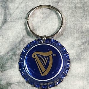 Pu&ograve; includere: Un portachiavi blu e argento con un tappo di bottiglia con il logo dell'arpa Guinness. Il tappo &egrave; blu con un disegno di arpa dorata e un portachiavi argentato.