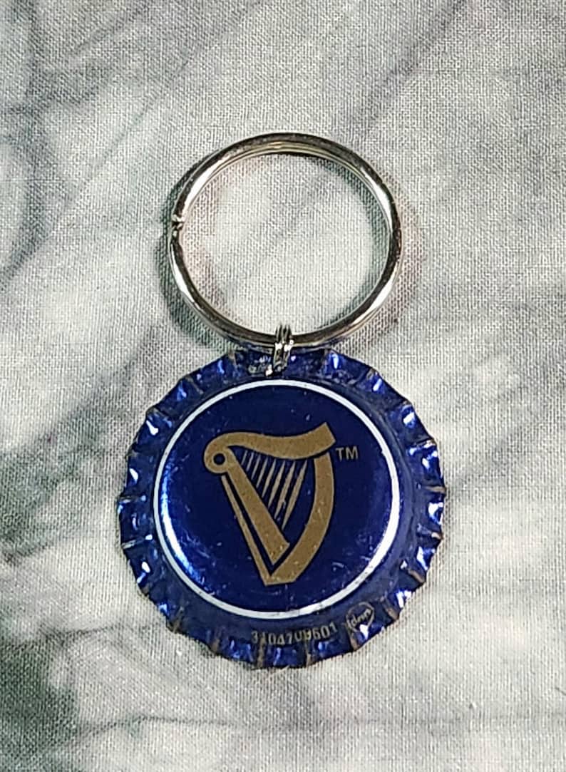 Pu&ograve; includere: Un portachiavi blu e argento con un tappo di bottiglia con il logo dell'arpa Guinness. Il tappo &egrave; blu con un disegno di arpa dorata e un portachiavi argentato.
