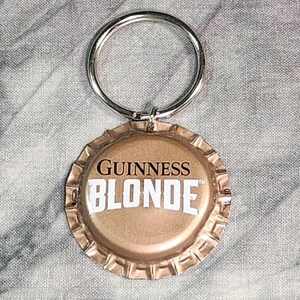 Pu&ograve; includere: Un portachiavi con un tappo di bottiglia di birra Guinness Blonde. Il tappo &egrave; color oro con le parole "GUINNESS BLONDE" in bianco. Un anello di metallo argentato &egrave; attaccato per le chiavi.