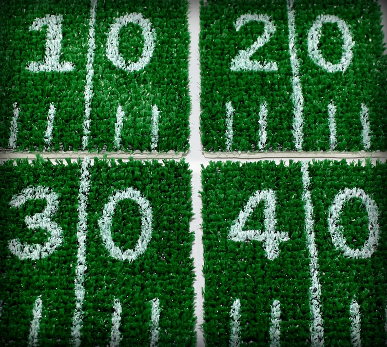 May include: Four green squares with white numbers 10, 20, 30, and 40 painted on them. The squares are made of artificial turf.