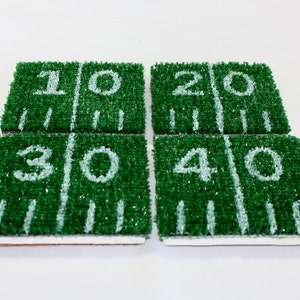 May include: Four green and white coasters with football field designs. The coasters are numbered 10, 20, 30, and 40.