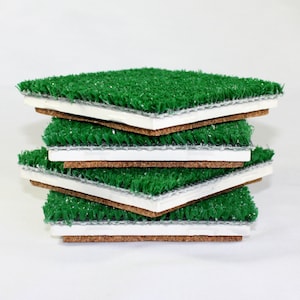 May include: A stack of four green artificial grass squares with a brown cork backing. Each square has a white foam layer between the grass and the cork.