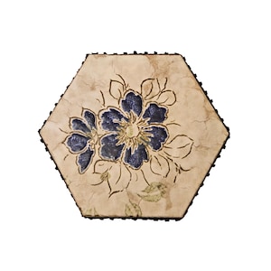 Può includere: Una piastrella in ceramica esagonale con una superficie color crema e una finitura smaltata a craquelé. Il centro presenta un motivo floreale dipinto a mano in blu profondo con contorni scuri, circondato da sottili accenti di foglie verdi.