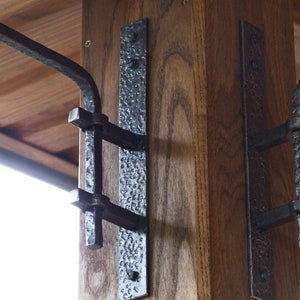 May include: A close-up of a wooden post with two black metal brackets attached to it. The brackets are designed to hold a railing or other structure.