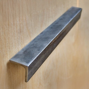 Peut inclure: Une poignée de porte en métal argenté de forme rectangulaire avec un léger pli au bas.