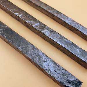 May include: Three long, thin, dark gray metal rods with a rough, textured surface.