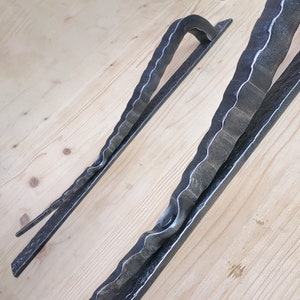 May include: Two black metal door handles with a wavy, textured design. The handles are made of forged iron and have a rustic, industrial look.