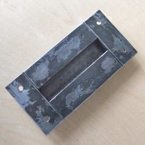 May include: A rectangular metal door handle with a brushed finish and four holes for mounting. The handle has a recessed area for a finger pull.