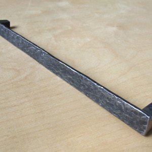 Peut inclure: Une longue poignée de tiroir rectangulaire en métal martelé avec des extrémités carrées. La poignée est de couleur gris foncé.