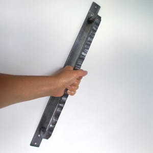 以下が含まれることがあります： 波打つようなテクスチャのある縁を持つ、長い銀色の金属製のドアハンドル。ハンドルは平らな金属プレートに取り付けられています。