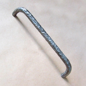 May include: A silver metal cabinet pull with a textured, hammered finish. The pull has a simple, curved design.
