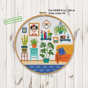 May include: A cross-stitch pattern in a wooden hoop, featuring a cozy living room scene. The design includes a Frida Kahlo portrait, potted plants, a blue cabinet, a yellow sofa, and the text "PDF PATTERN". The hoop is 8 inches in diameter.
