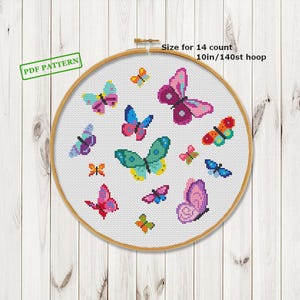 May include: A cross-stitch pattern with a collection of colourful butterflies in a range of sizes and patterns. The butterflies are stitched on white fabric, held within a wooden embroidery hoop. Text on the image reads "PDF PATTERN" and "Size for 14 count 25cm/140st hoop".