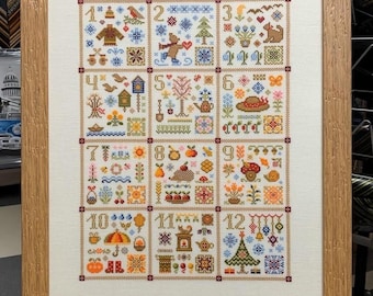 Könnte beinhalten: Ein gerahmter Kreuzstich-Sampler mit 12 verschiedenen Designs, die die Monate des Jahres darstellen. Jedes Design ist nummeriert und zeigt eine Vielzahl von Farben und Mustern.