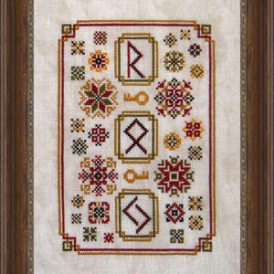 Op de afbeelding: Een witte kruissteekborduursel met een verscheidenheid aan kleurrijke geometrische patronen en symbolen, waaronder een sleutel, een ster en een bloem. Het borduursel is ingelijst in een bruin houten frame.