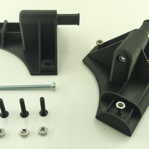 Könnte beinhalten: Schwarze 3D-gedruckte Kunststoffkomponenten, darunter zwei abgewinkelte Halterungen, Schrauben, Bolzen und Muttern. Die Teile sind auf einer weißen Oberfläche angeordnet, wahrscheinlich zur Montage oder Präsentation.