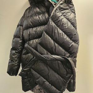 May include: A black puffer coat with a hood and a belt. The coat has a shiny finish and a snakeskin print lining in the hood. The coat is hanging on a hanger.