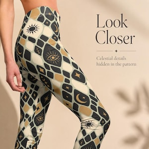Könnte beinhalten: Hoch taillierte Leggings mit einem sich wiederholenden geometrischen Muster aus abgerundeten Quadraten in Schwarz, Creme und Gold. Das Design enthält himmlische Motive wie Sonnen, Monde, Sterne und Augen. Der Text lautet Look Closer Celestial details hidden in the pattern.