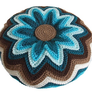 May include: A round crocheted pillow with a brown center and a blue flower design. The flower has multiple layers of petals in shades of blue and teal.