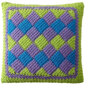 May include: A square pillow with a geometric pattern in shades of green, purple, and blue. The pillow is made of crocheted yarn and has a textured surface.
