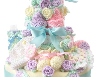 May include: A pastel-colored baby shower gift basket with crocheted items, including a frog, flowers, booties, and a hat. The basket is decorated with a blue ribbon and is presented on a white background.