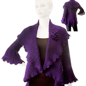 May include: Purple crocheted cardigan with a ruffled hem and bell sleeves. The cardigan has a shawl collar and a flower embellishment.