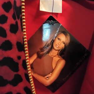 May include: Red fabric with black leopard print and a gold zipper. A tag features a photo of a woman in a brown top. The tag reads "GLOBAL CHIC".