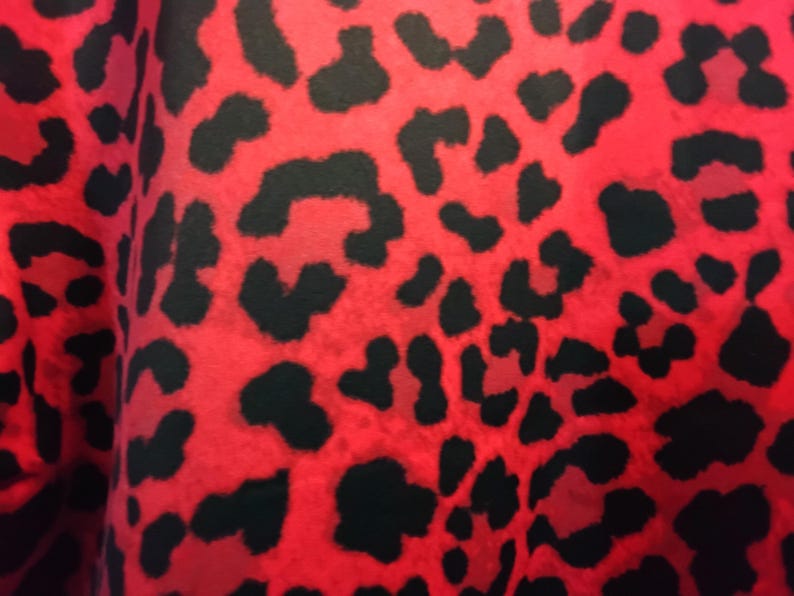 May include: Close-up of a fabric with a vibrant red background and black leopard spots. The pattern is bold and eye-catching, creating a striking visual texture. This textile is suitable for various fashion and design applications.