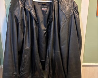 May include: Black leather jacket with a zip-up front, side pockets, and a buttoned collar. The jacket is hanging on a white hanger. The brand name "Reed" is visible on a tag inside the jacket.