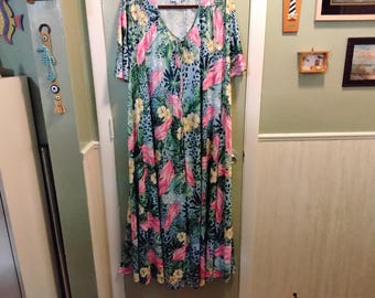May include: A long, flowing dress with a V-neck and short sleeves. The dress features a vibrant floral pattern with pink, yellow, and green leaves on a light blue background. The fabric appears soft and lightweight, suitable for warm weather.