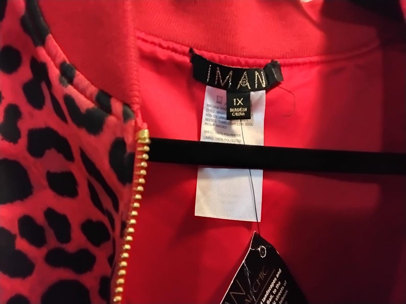 May include: A red bomber jacket with a black leopard print pattern. The jacket has a gold zipper and a red lining. The tag reads "IMAN" and "1X".