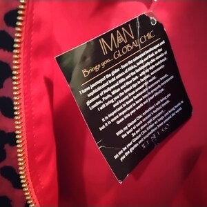 May include: Close-up of a red garment with a gold zipper and a black and red leopard print pattern. A black tag with the text "IMAN GLOBAL CHIC" is attached to the garment.