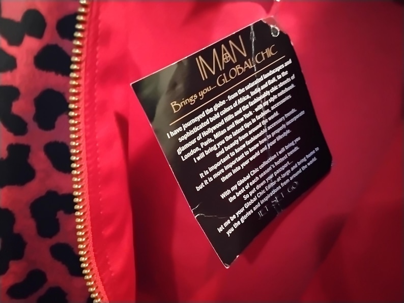 May include: Close-up of a red garment with a gold zipper and a black and red leopard print pattern. A black tag with the text "IMAN GLOBAL CHIC" is attached to the garment.