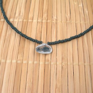 May include: A black beaded necklace with a silver pendant featuring a cloudy agate stone.