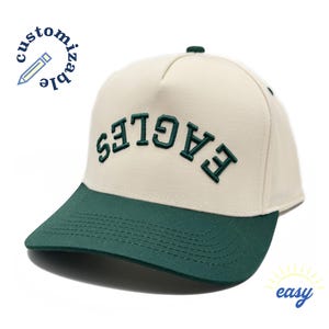 May include: A cream colored trucker hat with a green brim and the word "EAGLES" embroidered in green on the front.