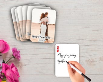 May include: A stack of personalized playing cards featuring a wedding photo and names. One card shows a hand writing "May your joining together". Pink roses are in the lower left corner. The cards have a rounded rectangle shape.