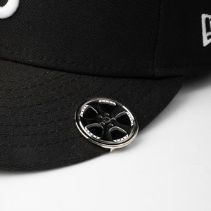 Puede incluir: Gorra de béisbol negra con un pin de rueda plateado y negro en el lateral.