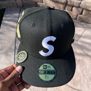 Peut inclure: Casquette de baseball noire et blanche Supreme New Era 59FIFTY ajustée avec un logo 'S' blanc sur le devant. La casquette a une visière noire et un logo New Era noir et or sur le côté. La casquette est de taille 7 1/4.