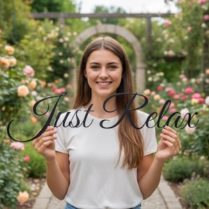 Pode incluir: Uma placa de metal preta com as palavras "Just Relax" em uma fonte cursiva. A placa é segurada em frente a uma mulher em uma camiseta branca, com um jardim de rosas ao fundo.