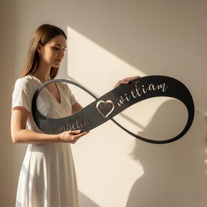 Peut inclure: Panneau décoratif en métal noir en forme de symbole infini, avec les noms "Isabella" et "William" en écriture cursive. Un cœur avec le mot "forever" est au centre.
