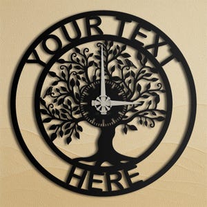 Könnte beinhalten: Schwarze Metall-Wanduhr mit einem Lebensbaum-Design. Das Zifferblatt zeigt einen Baum mit Blättern und zwei Vögeln. Die Wörter "YOUR TEXT" und "HERE" sind um das Zifferblatt herum ausgeschnitten.