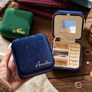 May include: Two small velvet jewelry boxes with gold zippers. The blue box has the name "Amelia" embroidered on the front. The green box has the name "Nova" embroidered on the front.