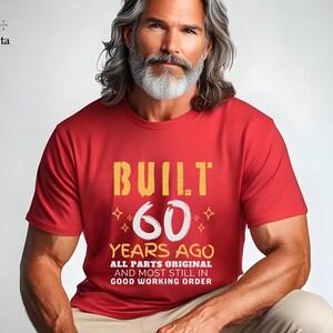 May include: Red t-shirt with the text "BUILT 60 YEARS AGO ALL PARTS ORIGINAL AND MOST STILL IN GOOD WORKING ORDER". The shirt has a distressed font in yellow and white.