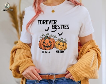 May include: A white short-sleeved t-shirt featuring the text FOREVER BESTIES in black, with an illustration of two orange jack-o'-lanterns and three black bats. The names OLIVIA and MARRY are printed in black below each respective pumpkin.