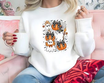 May include: White sweatshirt featuring a Halloween-themed graphic. The design includes cartoon ghosts, pumpkins with black and white plaid bows, spiderwebs, and a witch's hat. The sweatshirt has long sleeves and a crew neck.
