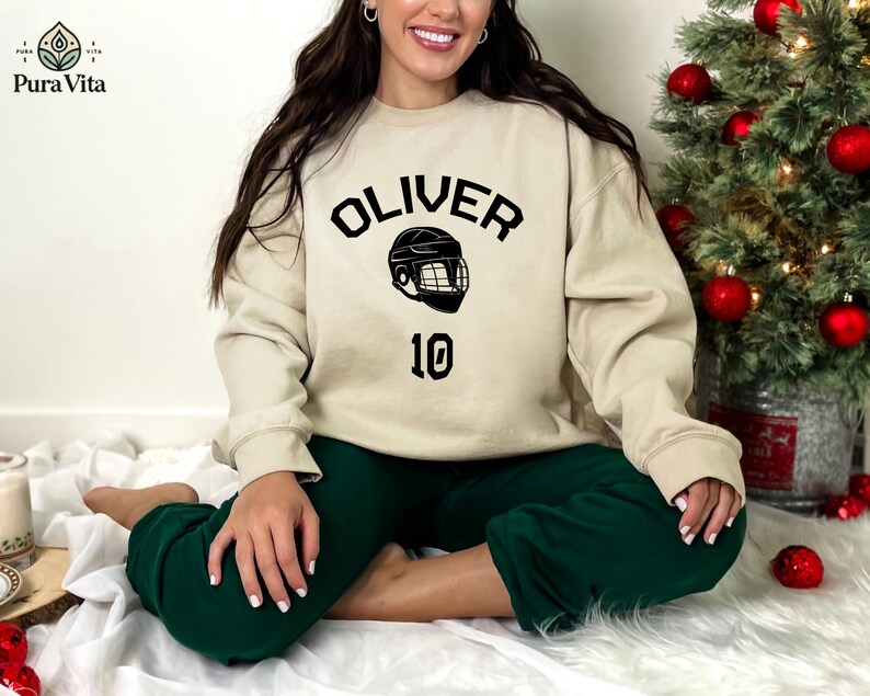 May include: A beige sweatshirt with black text that reads "OLIVER" and a hockey helmet graphic. The number "10" is printed below the graphic.